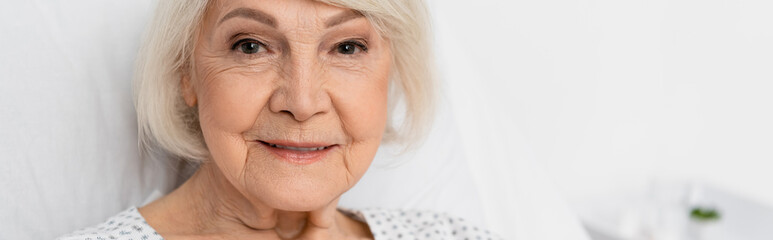 Senior woman smiling at camera in hospital ward, banner