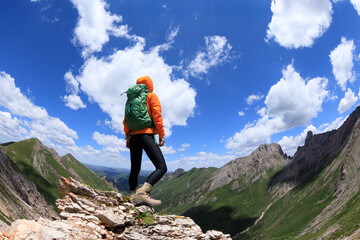 Successful woman backpacker hiking on sunset alpine mountain peak