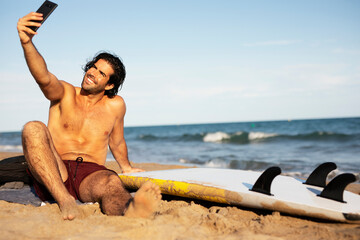 Portrait of handsome surfer with his surfboard. Young man taking selfie photo at the beach