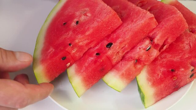 Man getting slices of ripe red watermellon on white plate. Picnic with slices of watermelon lying on the ceramic plate. Video 4k resolution.
