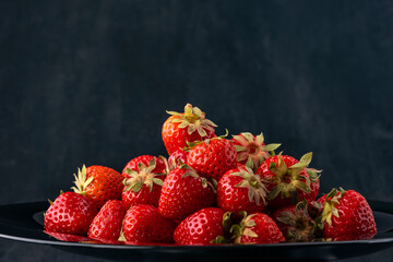 Ripe sweet strawberries on black background. Fresh summer berries, close up. Seasonal berries on a...