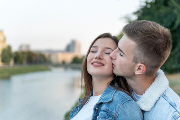 Portrait of young loving couple on river. Guy kisses his beloved on the cheek. Romantic date