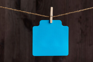Blank blue paper card hang with clothespin on rope. Copy space. Place for your text. Wooden background.