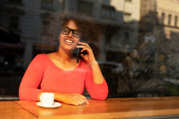 Young woman at cafe drinking coffee. Beautiful African talking to the phone while relaxing at cafe