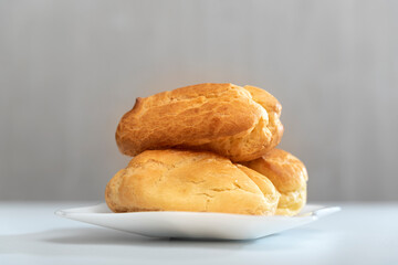 Homemade delicate profiteroles or eclairs without cream on saucer. Gray background.