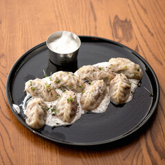 Boiled Dumplings with sour cream and herbs on black plate. Food plate on wooden table. Served dish. Soft focus.