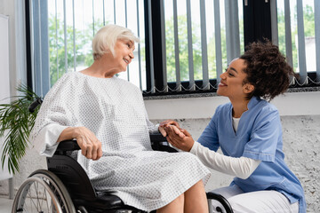 African american nurse holding hand of smiling elderly woman in wheelchair