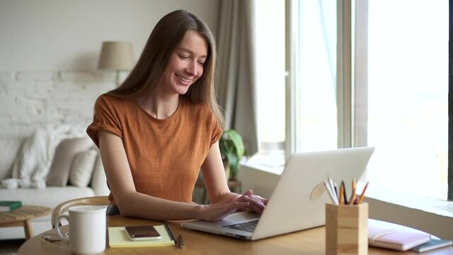 Smiling student types on laptop studying online at home