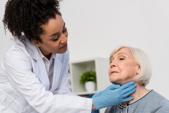 African american docktor in while coat checking neck of elderly patient