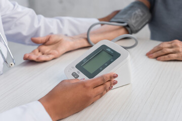 Cropped view of african american doctor holding electronic tonometer near blurred patient