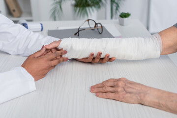 Cropped view of african american doctor touching and checking broken arm of patient