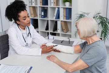 Obraz premium African american doctor pointing at plaster bandage on arm of patient