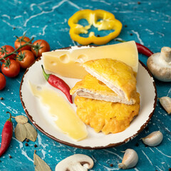 French poultry meat with cheese and pineapple. Plate with Baked or Fried chicken fillet with vegetables on blue table. Close-up shot. Soft focus.