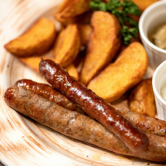 Close-up of fried sausages and potatoes with mayonnaise and mustard on clay plate. Simple rustic lunch. Junk food concept. Soft focus.