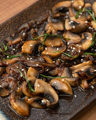 Fried mushroom slices on platter. Close-up shot of Clay plate with cooked champignons, herbs and sesame seeds. Soft focus.