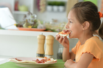 Little girl eating tasty pizza at home