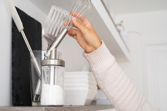 personne qui prend un fouet sur une etagere de cuisine 
