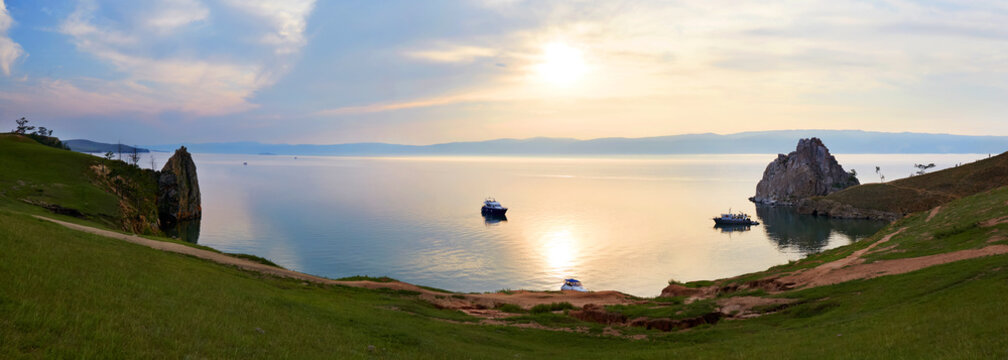 Sunset on Lake Baikal, Olkhon Island in summer. Panoramic view of the Khuzhir Bai and the Burhan chain, Shamanka or Shaman rock. Ships and yachts with tourists are resting in the bay.