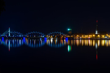 View of Riga (Latvia) in the evening. Old buildings and a railway bridge are illuminated and reflect in the Daugava river.