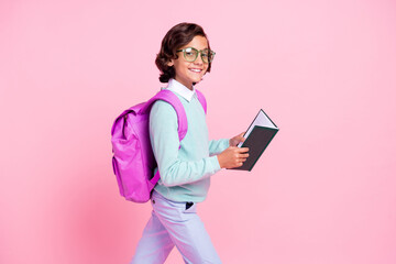 Photo of positive boy hold textbook read go wear eyewear backpack teal shirt isolated pink color background