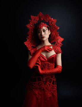 Full length  portrait of beautiful young asian woman wearing red corset, long opera gloves and ornate gothic queen crown. Graceful posing isolated on a dark studio background.