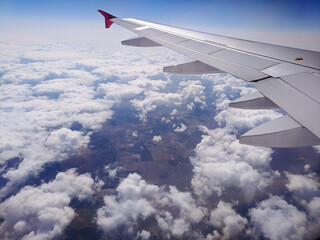 Obraz premium Beautiful window view of blue sky and fluffy clouds from passenger seat on airplane. View of many windmills at big green meadows. Concept of travel and air transportation.