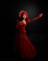 Fototapeta na wymiar Full length portrait of beautiful young asian woman wearing red corset, long opera gloves and ornate gothic queen crown. Graceful posing isolated on a dark studio background.