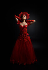 Full length  portrait of beautiful young asian woman wearing red corset, long opera gloves and ornate gothic queen crown. Graceful posing isolated on a dark studio background.