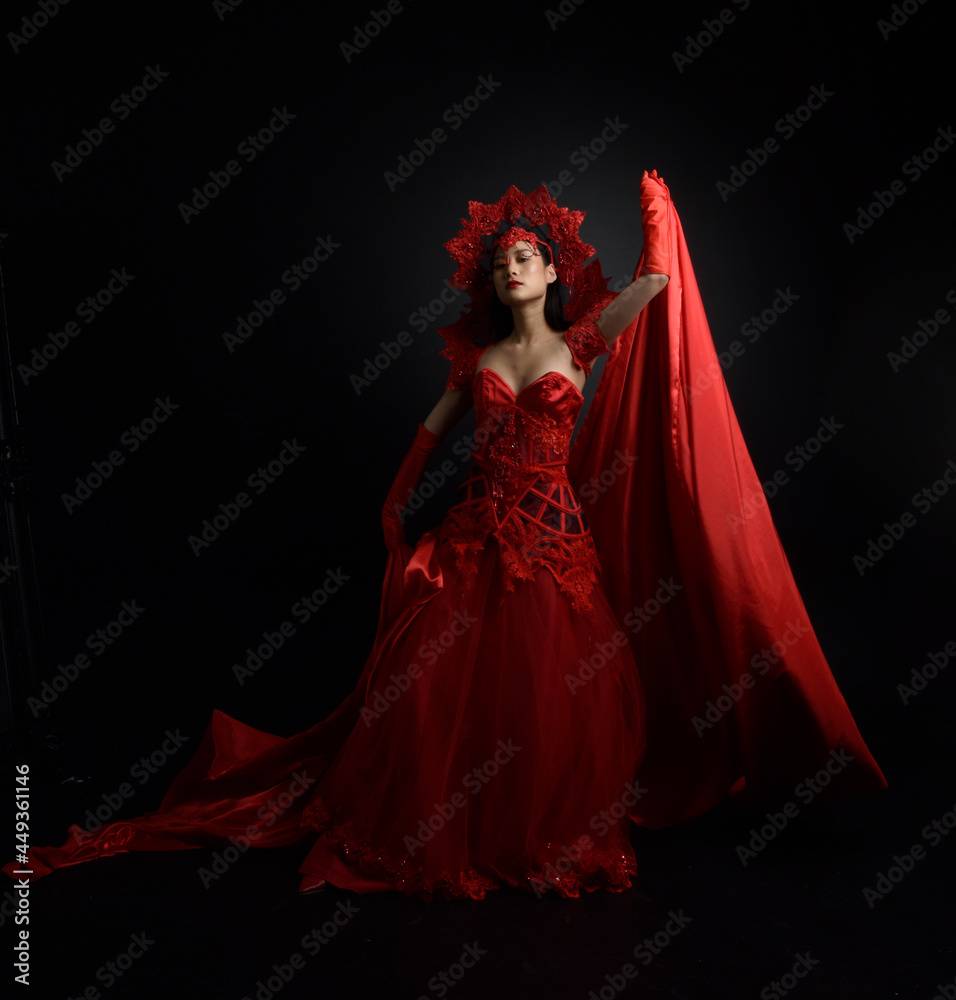 Wall mural Full length  portrait of beautiful young asian woman wearing red corset, long opera gloves and ornate gothic queen crown. Graceful posing isolated on a dark studio background. - Wall murals