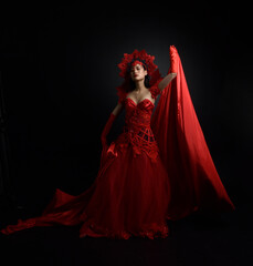 Full length  portrait of beautiful young asian woman wearing red corset, long opera gloves and ornate gothic queen crown. Graceful posing isolated on a dark studio background.