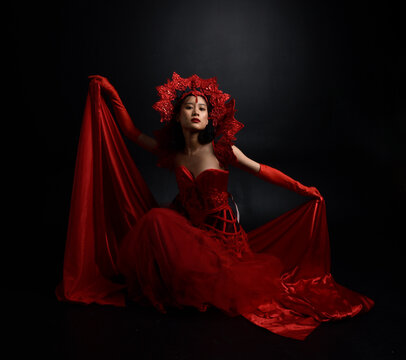 Full length  portrait of beautiful young asian woman wearing red corset, long opera gloves and ornate gothic queen crown. Graceful posing isolated on a dark studio background.