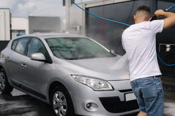 Back view of young man cleaning his car with a jet sprayer. Self-service car washing