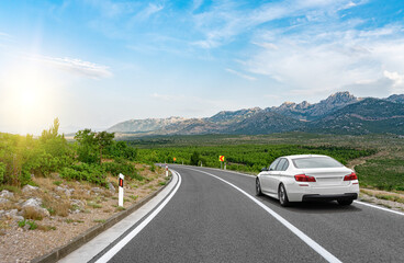 White car on a scenic road. Car on the road surrounded by a magnificent natural landscape. - obrazy, fototapety, plakaty