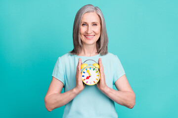 Photo of smiling cheerful mature lady grandmother hold clock time management isolated on teal color...