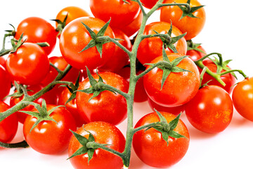Pile of red cherry tomatoes attached to their green branches on a neutral white background
