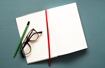 notebook with space for text, a red tab, glasses and a green pencil, on a painted background, photo from above 