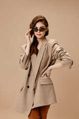 slender woman in coat and sunglasses on beige background cropped view