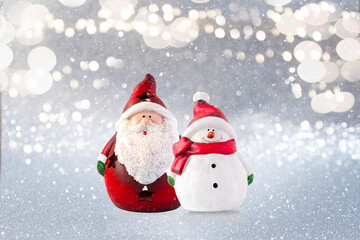 Santa and snowman christmas ornaments against silver glitter background with golden soft bokeh