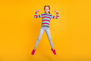 Photo of small girl jump show two strong biceps wear striped shirt jeans shoes isolated yellow color background