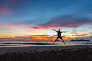 A happy man jump during beautiful twilight sunset on beach
