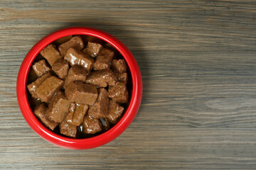 Wet pet food in feeding bowl on wooden background, top view. Space for text