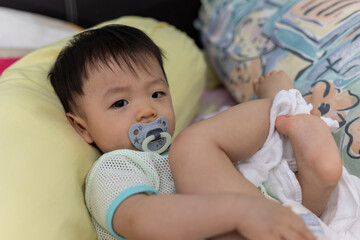 Portrait image of cute baby boy with sucking pacifier lying on bed