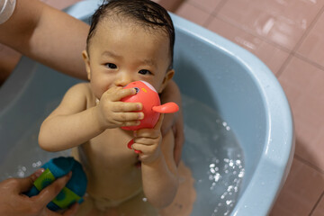 adorable baby boy taking bath in blue tub with toy on hand