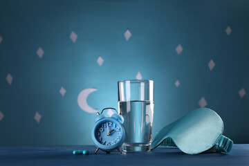 Alarm clock, soporific pills and sleeping mask near glass of water on table against blue wall...