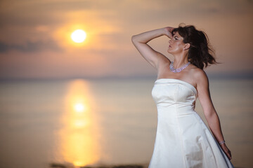 Fototapeta na wymiar Beautiful bride in white wedding dress at sunset near a beach and the ocean or sea coast in United Kingdom