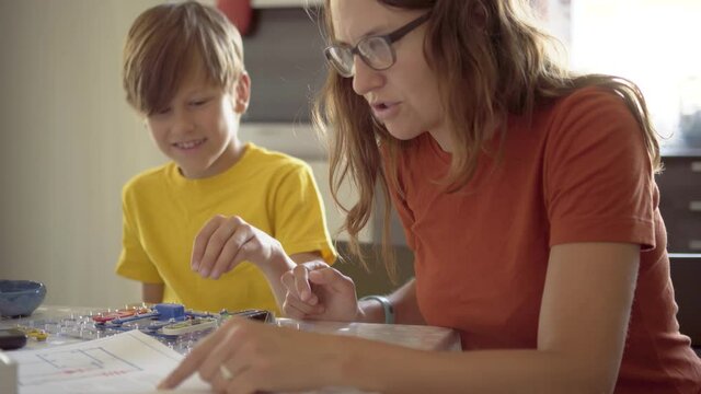 Mother plays with son. The family spends time together playing games with the construction set. The child enthusiastically collects electrical circuits. Robotics classes at home with parents.