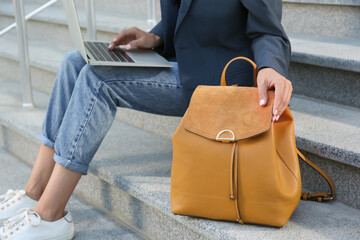 Young woman with stylish backpack working on laptop outdoors, closeup