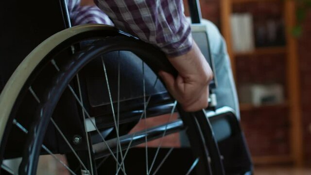 Closeup of male hand turning wheels of wheelchair. Closeup rolling wheelchair with disabled in home, back view. Concept treatment paralysis