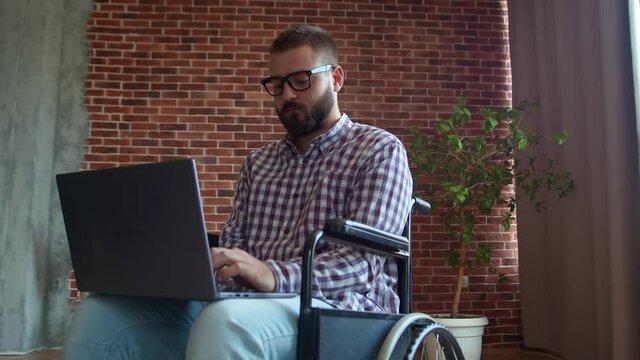 Man in wheelchair working with laptop at home. Handicapped invalid paralysed freelancer, immobilized entrepreneur working from home, ilness and disability