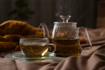 Tray with cup of hot tea and teapot on bed
